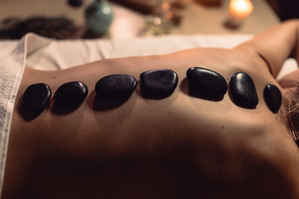 Person som utför en hot stone massage behandling med svarta varma stenar på sin rygg.